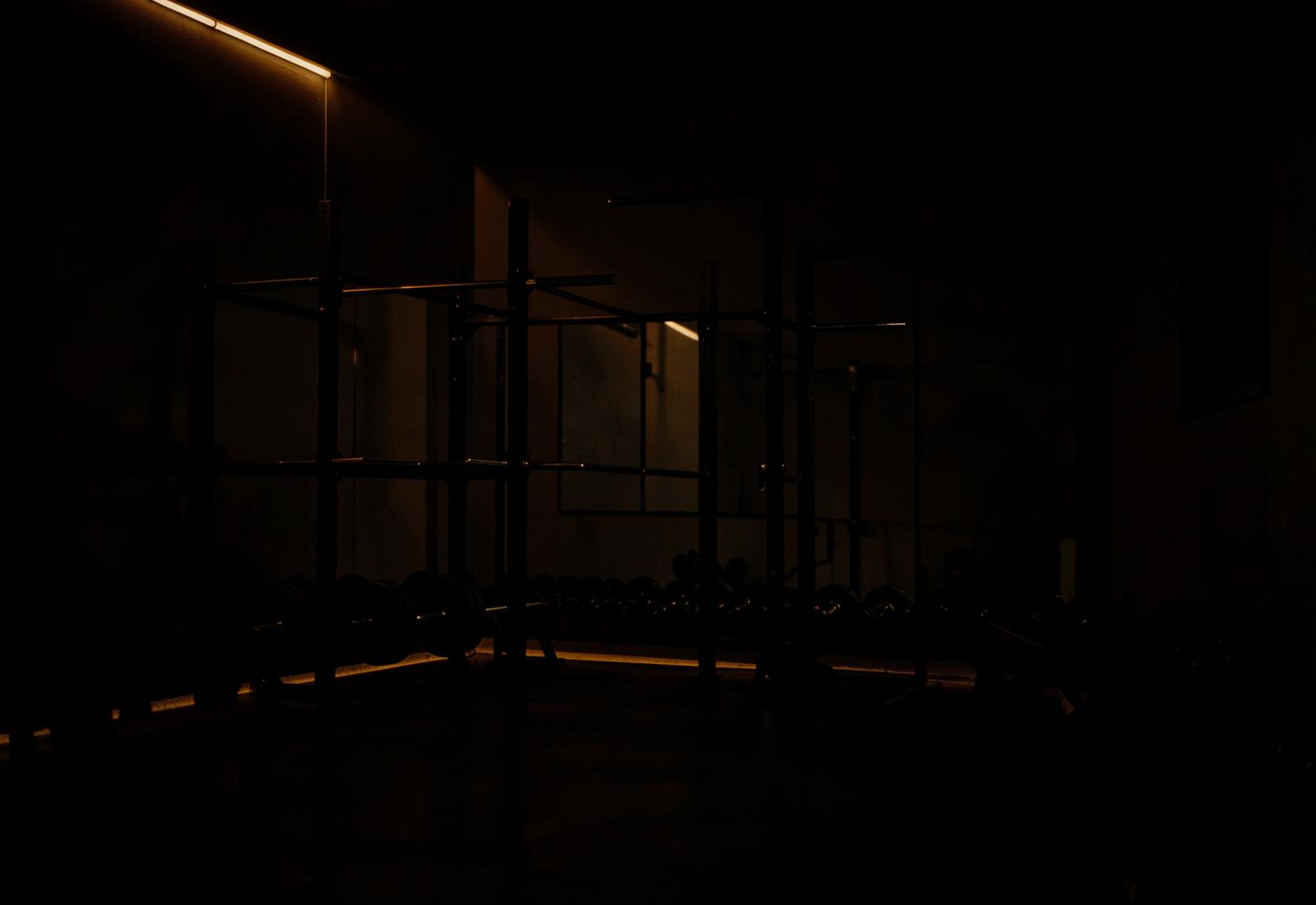 Dimly lit gym with a squat rack and dumbbells